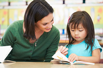 A kid with a book and a woman looking over the kids shoulder.