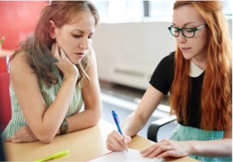 Two teenage students sitting at a shared desk writing and collaborating