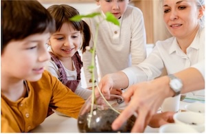 Three young students and their teacher observing a seedling plant in a glass test tube