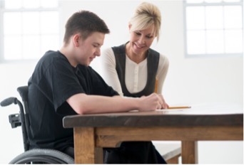 Educator seated at a table with a young adult in a wheelchair
