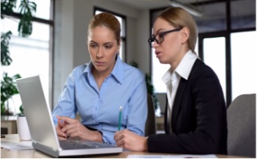 Two female professionals seated at a table, looking at a laptop