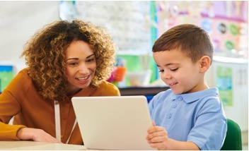 Woman helping young boy with a tablet in a classroom