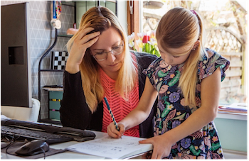 Woman helping elementary-aged girl with homework at a table