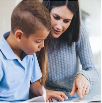 A young boy and a female teacher point at the page of a book as they read together
